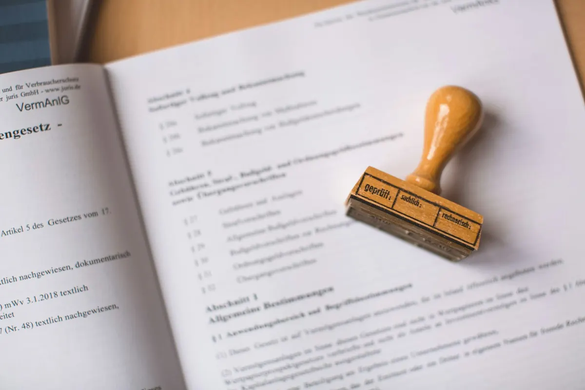 A German legal document open on a desk with a wooden rubber stamp lying on the page