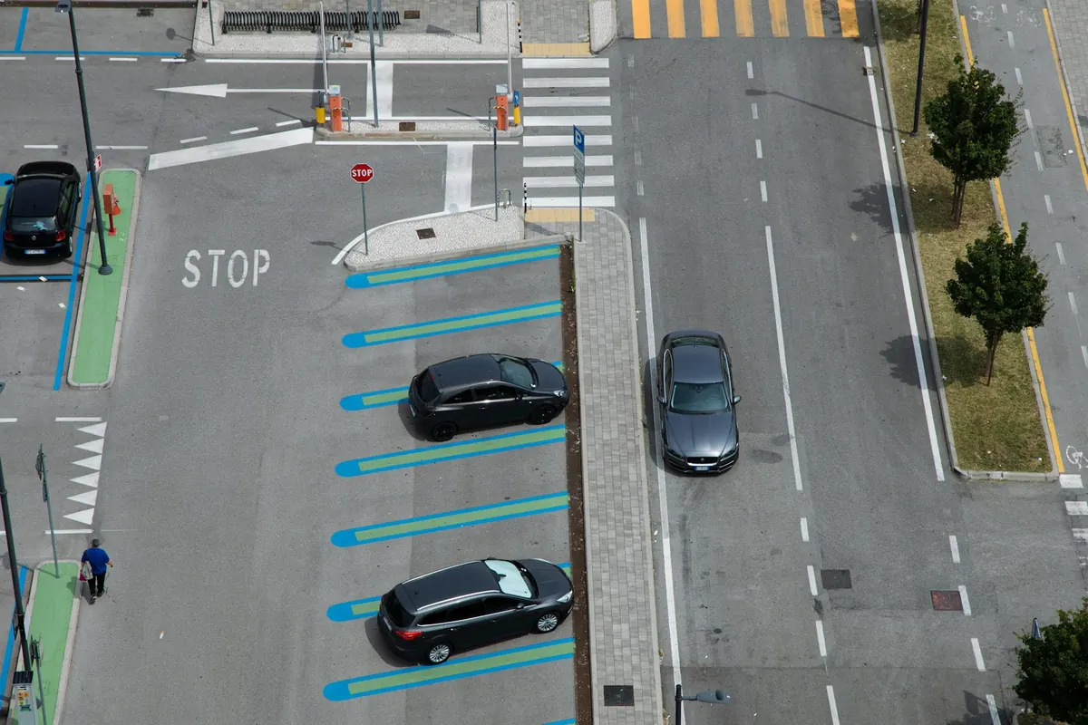 Overhead view of a street and parking lot, with bounding boxes drawn around three cars, a pedestrian and a stop sign
